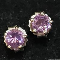 Close-up of sterling silver stud earrings each set with faceted round-cut amethyst stones with scalloped edge silver settings.