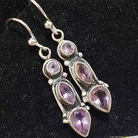 Close-up of the front of the sterling silver earrings showing three amethyst stones each with details of the stone cuts and settings.