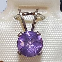 Close-up front view of sterling silver amethyst pendant, showing round purple faceted stone and sterling silver setting with four prongs.