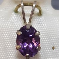 Front view of oval-shaped amethyst pendant with silver prongs and bail.