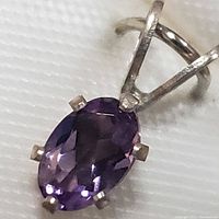 Close-up top view of an oval faceted amethyst gemstone set in a sterling silver pendant with a bail for chain attachment.