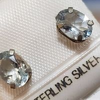 Close-up photo showing the pair of sterling silver earrings featuring faceted oval aquamarine stones in prong settings, displayed on a card labeled 'Sterling Silver'.