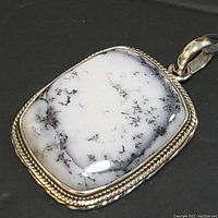 Close-up of rectangular white dendrite opal with black dendritic inclusions set in ornate sterling silver bezel pendant.