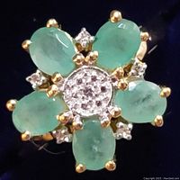 Close-up front view of sterling silver ring with five oval green emeralds and diamond accents in cluster design.