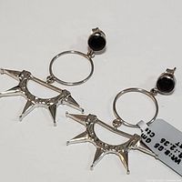 Pair of sterling silver earrings featuring circular hoops with attached spiked silver fan-shaped elements and round garnet stones on the stud part.