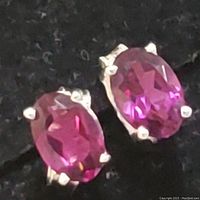 Close-up of pair of sterling silver earrings with oval-shaped garnet gemstones in prong settings against black background.