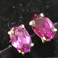 Close-up front view of two oval faceted garnet stones set in sterling silver prong settings, showing deep pink/red color and sparkle.