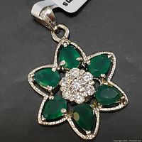 Front view close-up of sterling silver flower-shaped pendant with six green onyx petals and central cluster of clear stones on black background.
