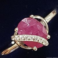 Close-up view of the ring showing the ruby-colored stone, cubic zirconia accents, and silver band detail.