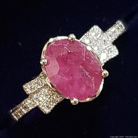 Close-up of oval faceted ruby set on sterling silver band with pavé clear stones on shoulders