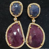 Close-up front and side views of drop earrings showing faceted rubies and sapphires bordered by small clear stones in sterling silver.