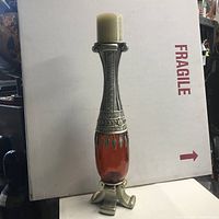 Full view of tall decorative candle stand with candle on top showing amber body and silver-tone metal accents.