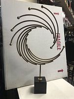 Full view of decorative metal abstract sculpture on granite base showing spiral curved rods with spherical ends.