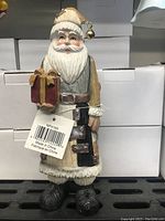 Front view of Father Christmas figurine showing gift in one hand and detailed face and coat textures with a metallic bell on the hat.