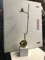 Side view of the full golden tree branch sculpture with bird perched near the top and hand base resting on white pedestal.