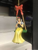 Close-up image of the Snow White figurine on a swing with red bow detail.
