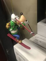 Front side view of colorful Disney Goofy skiing ornament hanging with gold string.