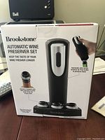 Front view of the box showing the product name, image of the wine preserver pump, and stoppers with details about functionality.