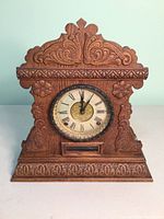 Front view of the antique carved wooden mantle clock with Roman numeral dial and ornate carved decorations.