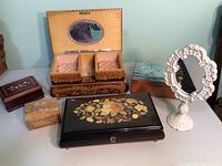 Photo of five assorted jewelry boxes and a small freestanding white oval mirror arranged on a flat surface against a pale green wall.