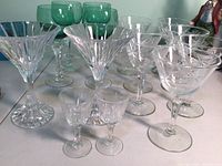Front view of the stemware including green wine glasses, star pattern martini glasses, two unique martini glasses, cordials and martini shakers.