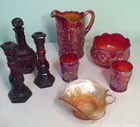 Full set of Avon dark red glass decanter, candlestick holders, and Carnival glass pieces shown together