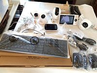 Two Dell keyboards and computer mice in packaging, several baby monitors and security cameras on tabletop.