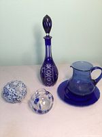 Full view of all five items including the tall cobalt decanter, pitcher with plate, and three art glass pieces.
