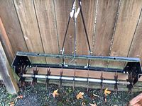 Front view of the lawn aerator attachment showing the aerator tines and bottom frame with signs of wear and rust.