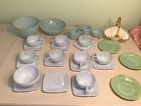 Complete set of blue milky Fire King cups and square saucers displayed with two larger blue bowls, creamers, jadeite saucers, and milk glass basket.