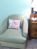 Front view of mint green swivel armchair with a pastel patchwork pillow on it, positioned near a wooden side table with a lamp.