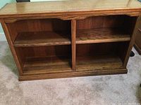 Front view of oak wood low wide bookcase with two open shelves separated by a vertical divider