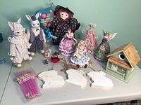 Overview of lot items showing large Easter bunny figurines, Halloween doll, carved angel, birdhouse, small figurines, bunny silhouettes, and Frozen straws