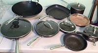 Multiple granite stone cookware items, including skillets, pots, lids, and a wok seen on table.