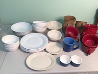 Overview of the lot including white plates, bowls and multicolor mugs