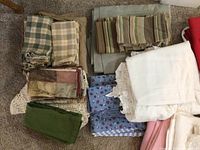 Overview of assorted folded fabrics showing variety of colors and patterns including green, beige, striped, floral print, and blue flower pattern