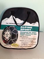 Full front view of black carrying bag labeled Alpine Sport Premium Tire Chain with white mountain graphic and product details.
