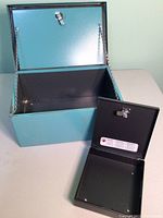 Open large turquoise metal lock box showing interior and hinged lid with chain supports.