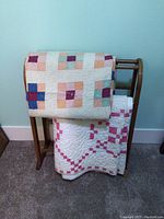 Two vintage quilts draped on wooden quilt rack showing general view of lot