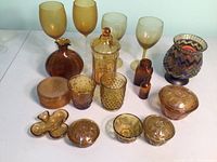 Full view of the assortment of vintage amber glass items including wine glasses, lidded jars, decorative vase, candle holder, and small bottles.