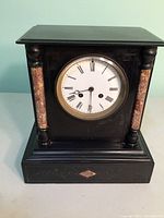 Front view of the vintage black marble mantle clock showing Roman numeral dial and pink marble columns.