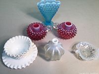 Full view of all pieces showing cranberry hobnail candlesticks, milk glass bowl and saucer, turquoise glass, opalescent bowl, and small perfume bottle.