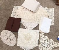 Photo showing assorted crocheted doilies, cloth napkins in brown and white, and a large cream crocheted table runner.