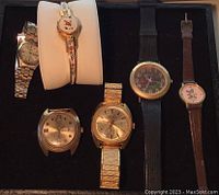 Overview shot showing all six wristwatches in the lot arranged on black surface, with different band types and dial styles visible.