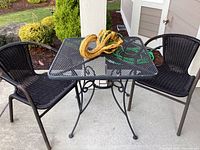 Outdoor black metal mesh bistro table with two black woven chairs and a colorful gourd on the table