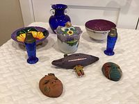 Overview of lot showing vintage cobalt blue glass salt and pepper shakers, blue glass vase, three glazed ceramic bowls, and three clay wall sculptures including two masks and a fish-shaped piece.