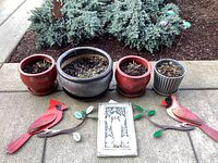 Photo shows four ceramic planters arranged on a sidewalk patio, with two red cardinal yard art figures and a framed tile art piece in front.