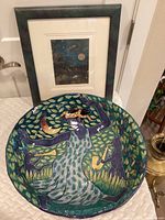 Front view of the ceramic bowl showing the dancing woman and animals while the framed art is in the background