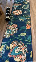 Full view of rolled floral runner rug on floor alongside non-skid pad.