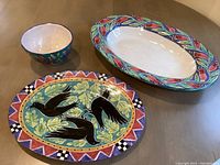 Photo showing all three pottery pieces together: large platter with black birds and oak leaves, large oval serving bowl with floral design, and small floral bowl.